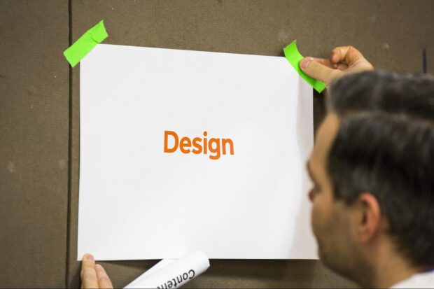 Picture of a white paper stuck on a wall with the word 'design' printed on it in the centre.