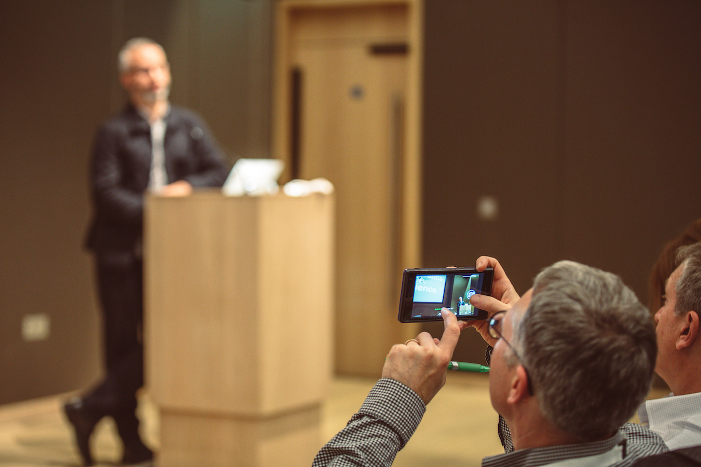 A man standing at a lectern and being photographed by another man