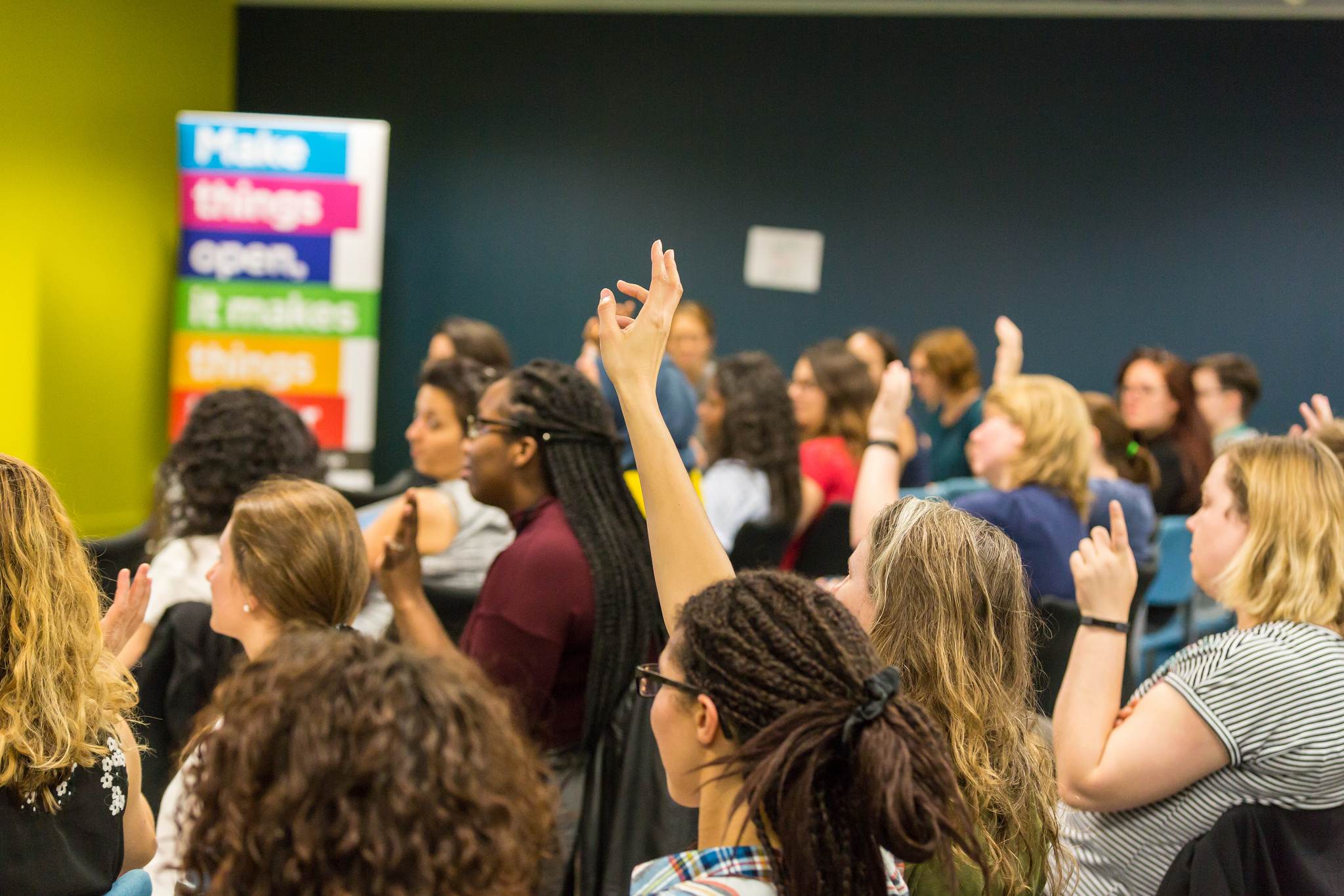 An image of people with their hands raised in the audience of a show and tell