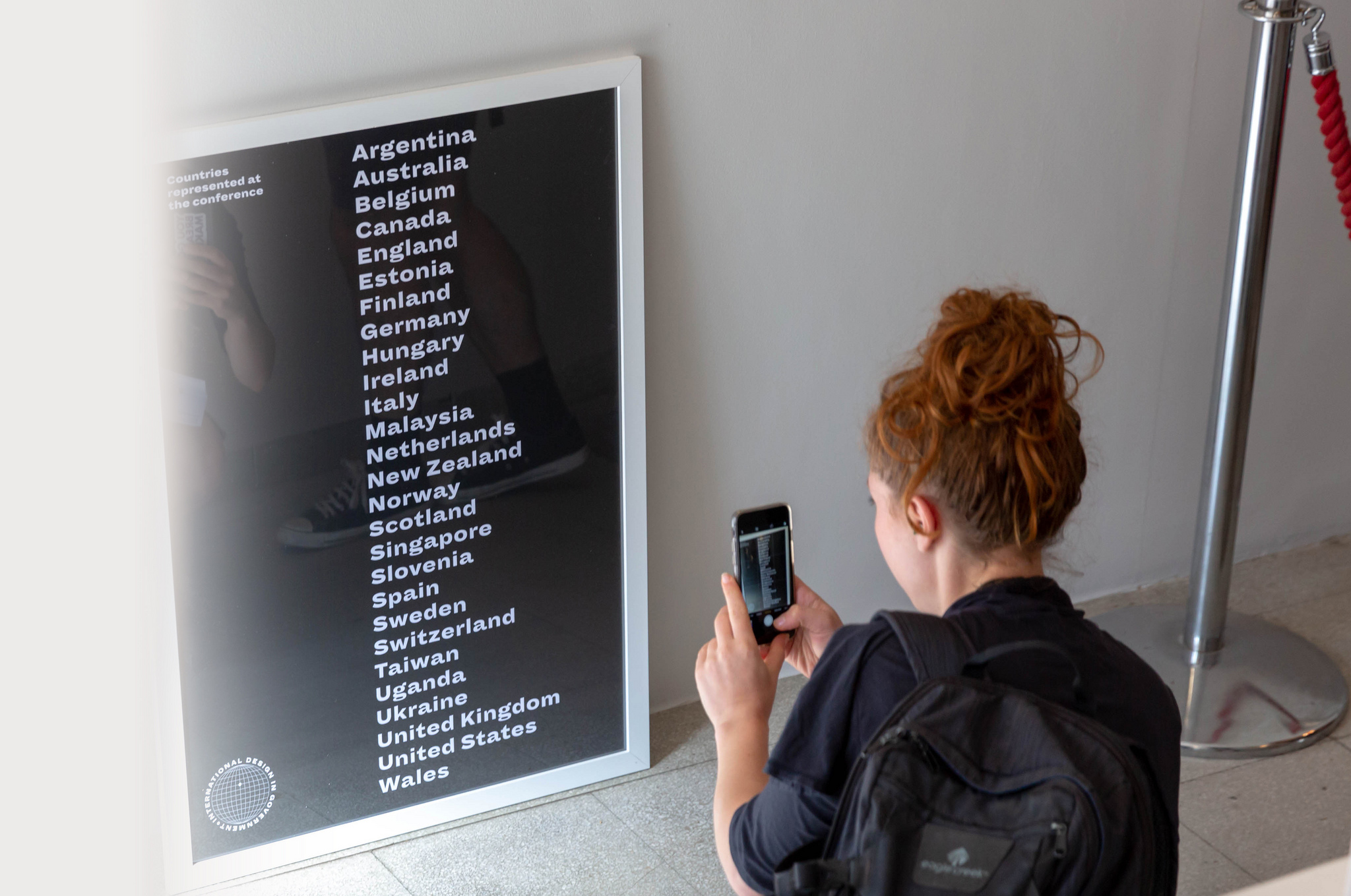 A woman taking a photograph of a black-and-white poster