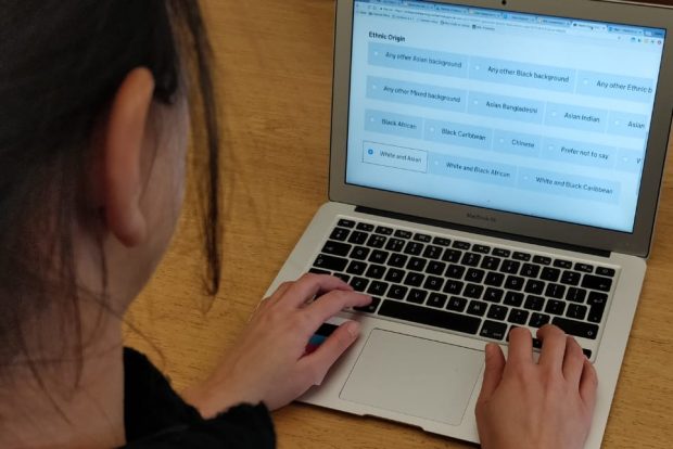 A person working on a laptop - the screen is showing a service where the user's ethnicity is being asked