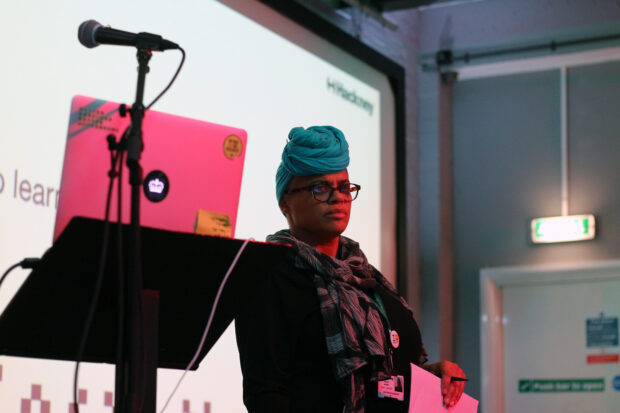 Joanne Moore, service design lead at Hackney Council, standing next to a computer and microphone while overseeing a workshop during a cross-government service design meetup, co-run with Hackney Council