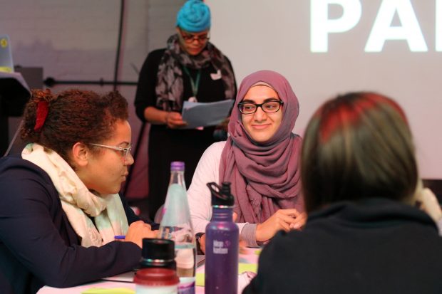 A small group of woman with different darker skin tones participating in a cross-government workshop, working with coloured sticky notes