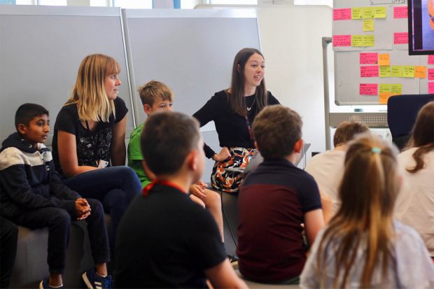 Carolina Pizatto, service designer at the Ministry of Justice, speaking in front of a group of kids of different ethnicities, surrounded by whiteboards with colourful stickie notes