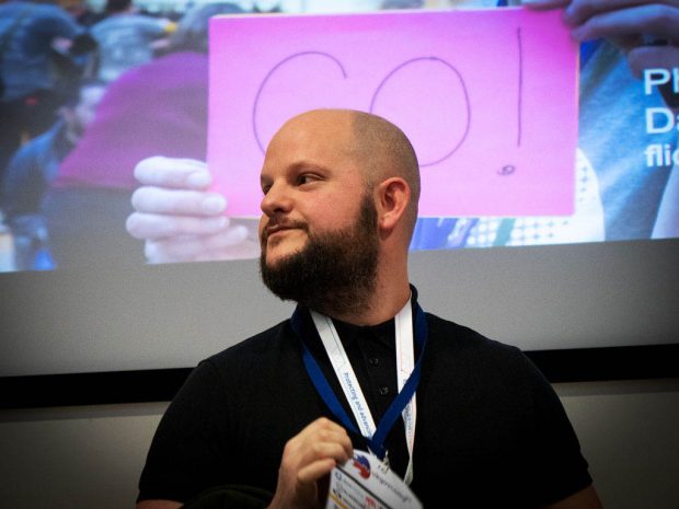 Rob King, interaction designer at the Ministry of Justice, standing in front of a large projection wall at a design event