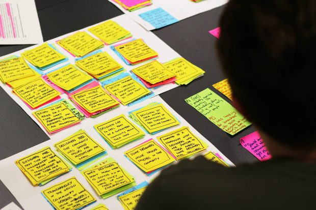 Small piles of sticky notes on a table, clustered and summarised with a person looking at them