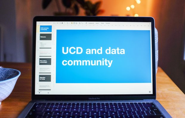 A computer standing in a room, its screen shows a slidedeck reading ‘UCD and data community’