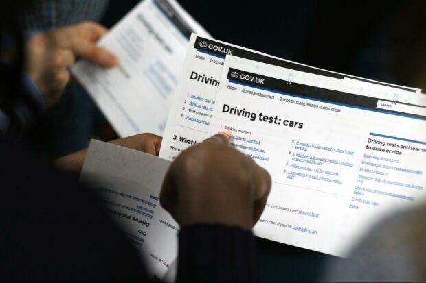 2 people standing next to each other holding print-outs of service pages from GOV.UK; in the foreground, a black woman pointing at ‘booking your test’, part of driving test service for cars