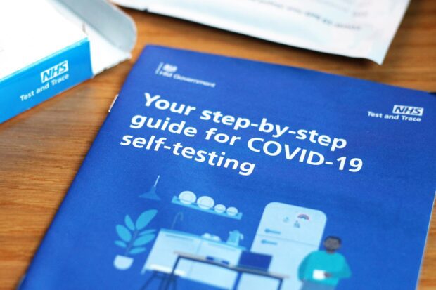 An instructions for use booklet of NHS Test and Trace rapid lateral flow tests on a table next to an opened test kit