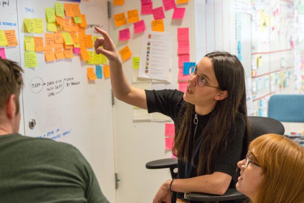 3 young designers discussing their work in front of a wall full of colourful stickie notes