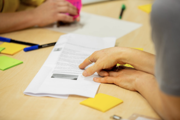 2 people discussing a bit of content, which is printed out. They have post it notes and pens to add notes to the content.