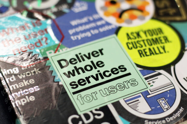 A laptop with a lot of stickers. In focus is a sticker which says 'Deliver whole services for users'