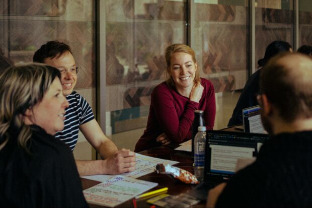 People sitting around a table looking at another person presenting something.