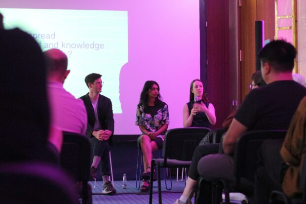 3 people talking in front of an audience in a purple lit space – 1 man and 2 women.