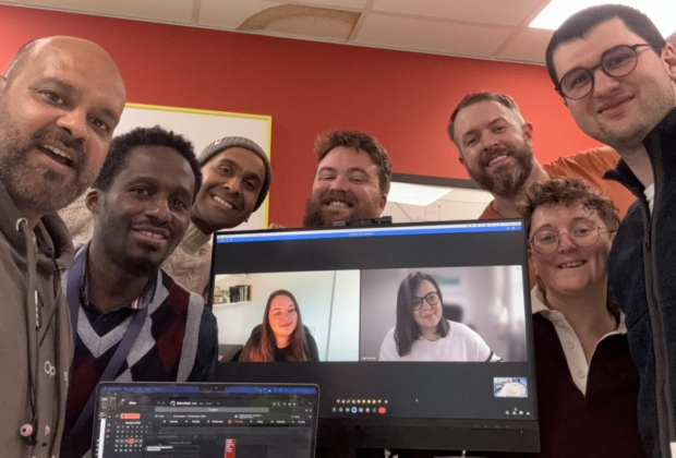 The VOA team posing for a photo around a desktop screen. 2 team members are on the screen. The other 7 people are in a room together.