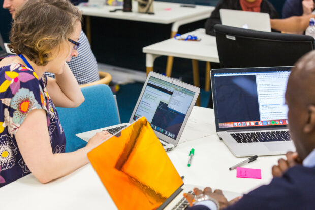 2 people sat at a table with their laptops discussing code